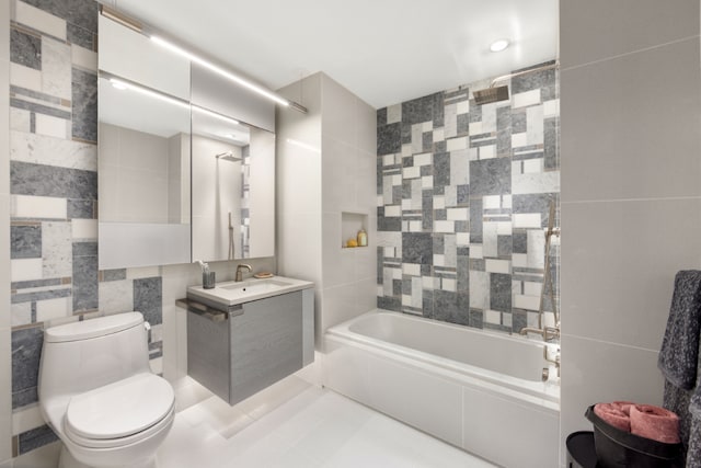 full bathroom with toilet, tiled shower / bath combo, tile patterned flooring, tile walls, and vanity