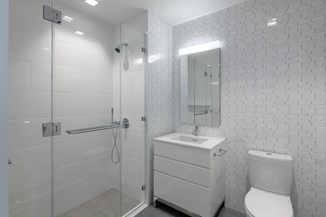 bathroom with vanity, toilet, a shower with shower door, and tile walls