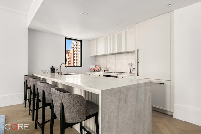 kitchen featuring light parquet floors, light stone countertops, white cabinets, a breakfast bar, and sink