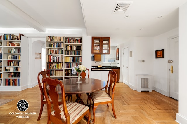 dining space with beam ceiling, sink, and light parquet floors