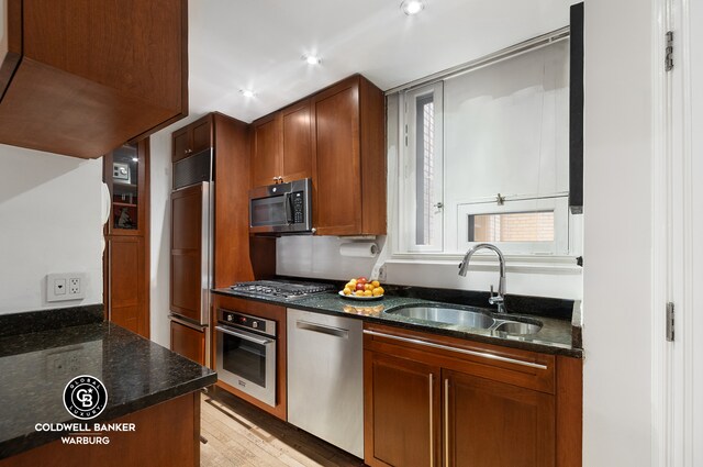 kitchen with appliances with stainless steel finishes, dark stone countertops, light hardwood / wood-style flooring, and sink