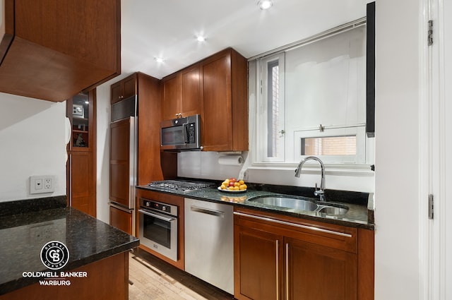 kitchen with dark stone counters, stainless steel appliances, light wood-type flooring, a sink, and recessed lighting