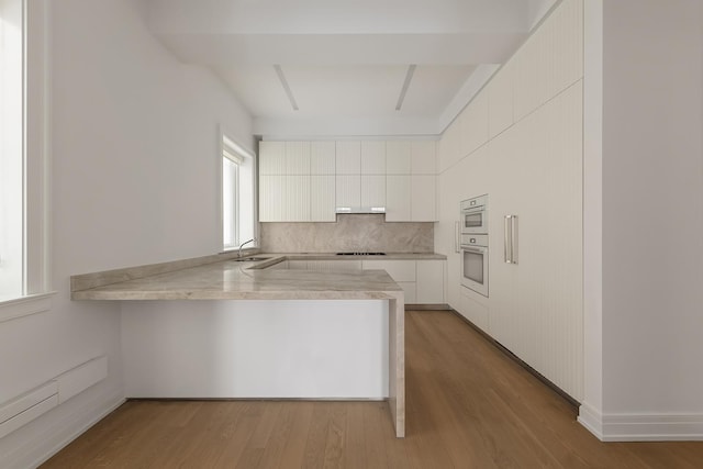 kitchen featuring a peninsula, stovetop, a sink, light countertops, and white cabinets