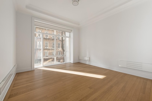 spare room featuring visible vents, a tray ceiling, baseboards, and wood-type flooring