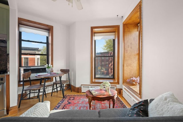 living area with light wood-type flooring, baseboard heating, a healthy amount of sunlight, and ceiling fan