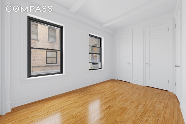 spare room with cooling unit, beamed ceiling, baseboards, and light wood-style flooring