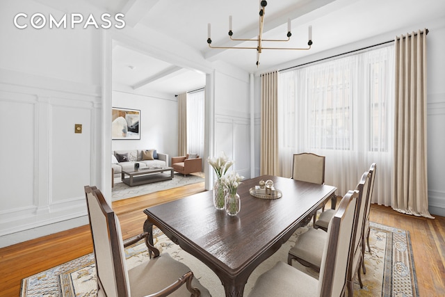 dining space featuring a notable chandelier, a decorative wall, beam ceiling, and wood finished floors