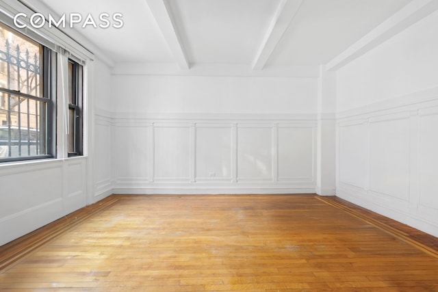 spare room with beamed ceiling, a decorative wall, and light wood-type flooring