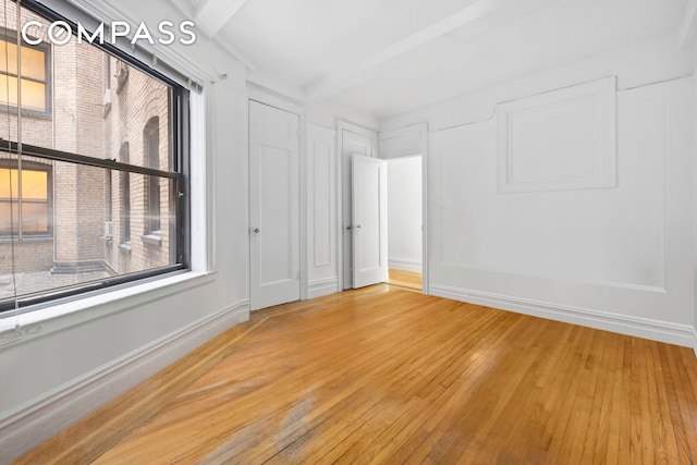 unfurnished room with beamed ceiling, baseboards, and light wood finished floors