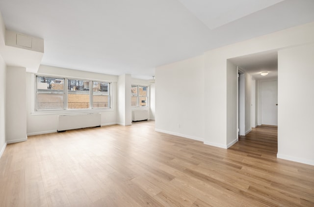 unfurnished living room featuring radiator heating unit and light wood-type flooring