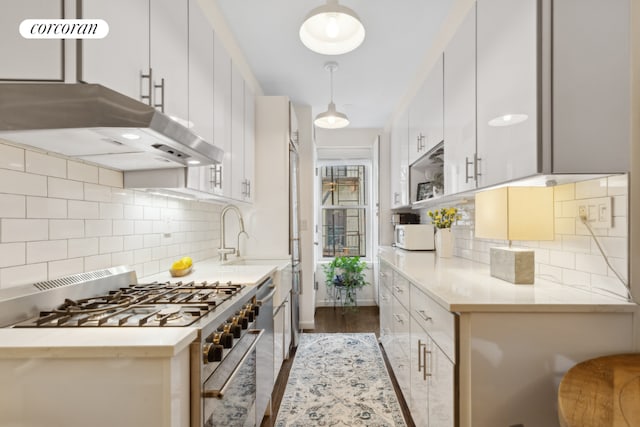 kitchen with pendant lighting, white cabinets, tasteful backsplash, and high end range