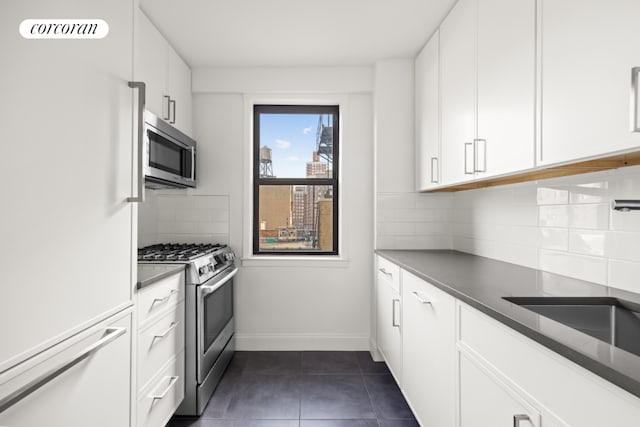 kitchen with backsplash, white cabinets, stainless steel appliances, and dark tile patterned floors