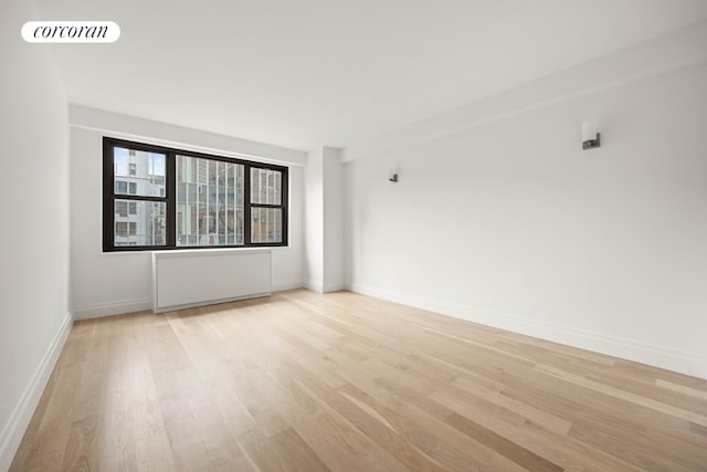 unfurnished room featuring radiator and light wood-type flooring