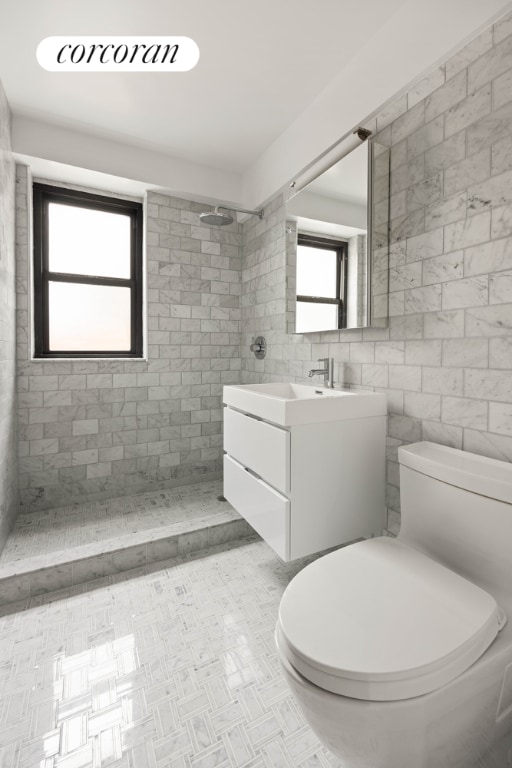 bathroom featuring vanity, toilet, tile walls, and tiled shower