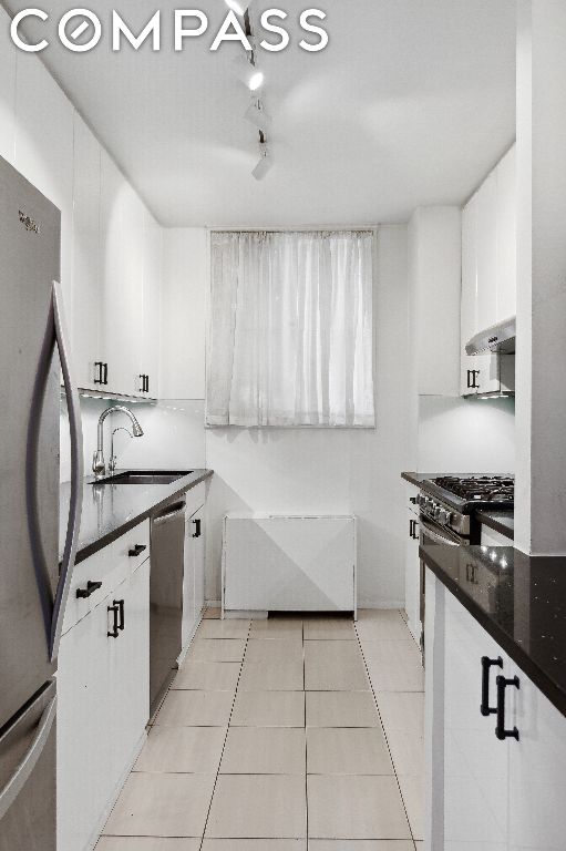 kitchen featuring white cabinetry, stainless steel appliances, dark stone countertops, sink, and light tile patterned floors