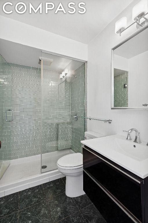 bathroom featuring toilet, a shower with door, and vanity