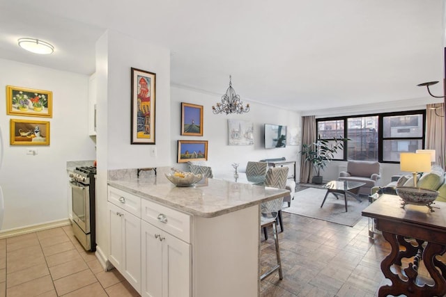 kitchen featuring stainless steel gas range, a breakfast bar area, light stone counters, a chandelier, and white cabinets