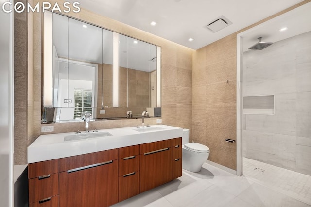 bathroom featuring toilet, tiled shower, tile walls, tile patterned floors, and vanity