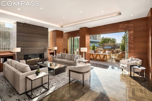 living room with a fireplace, a raised ceiling, wooden walls, and parquet flooring