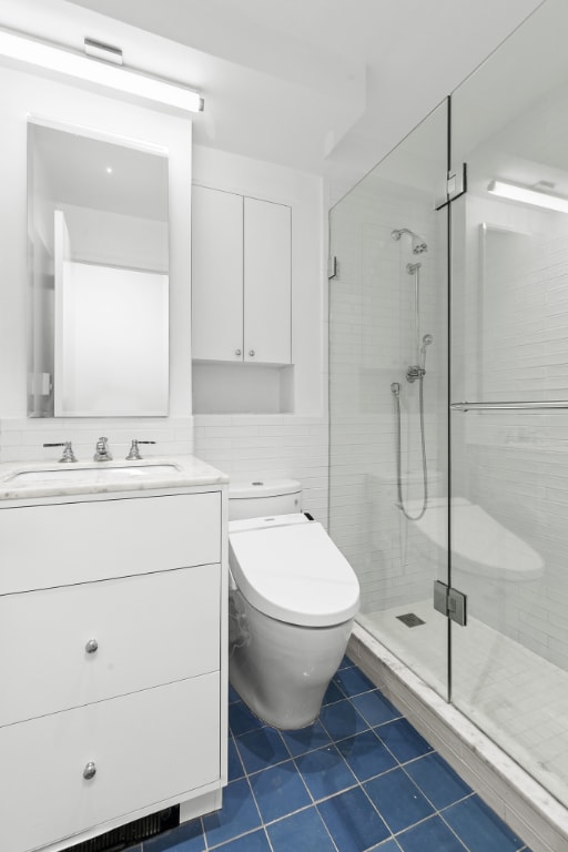 bathroom featuring tile patterned floors, toilet, tile walls, vanity, and a shower with door