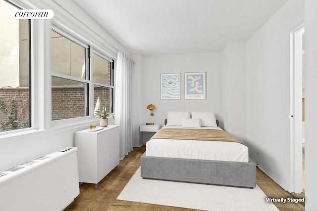 bedroom featuring light parquet flooring, radiator, and a textured ceiling