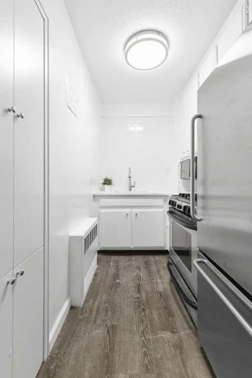 kitchen with a textured ceiling, white cabinets, radiator heating unit, dark wood-type flooring, and stainless steel appliances