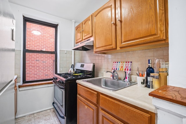 kitchen featuring decorative backsplash, sink, white refrigerator, and stainless steel gas range oven