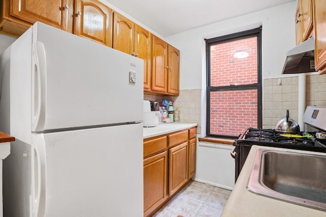 kitchen with white fridge, stainless steel gas range, tasteful backsplash, and sink