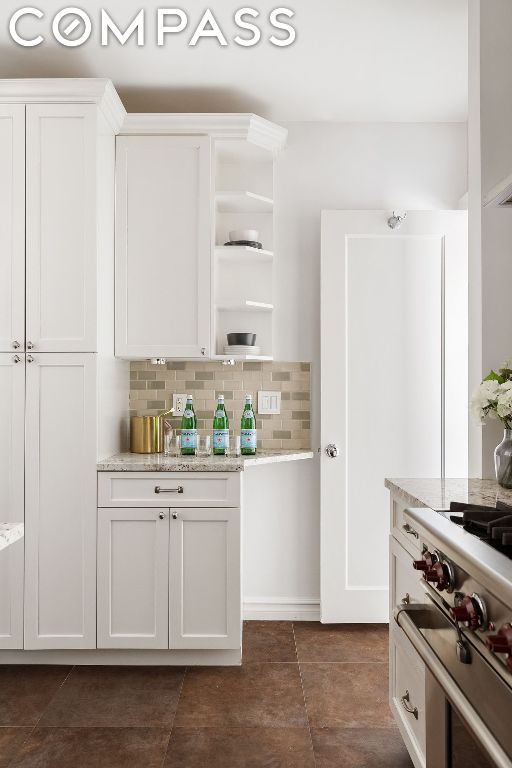 kitchen featuring white cabinetry, tasteful backsplash, light stone counters, and dark tile patterned flooring