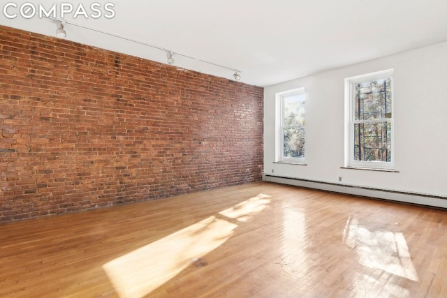 unfurnished room with rail lighting, brick wall, baseboard heating, and light wood-type flooring