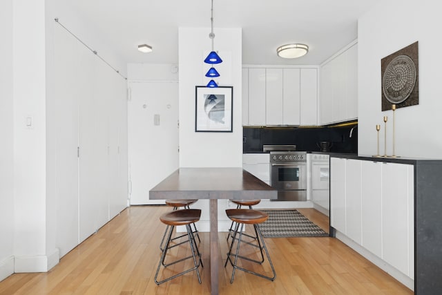 kitchen featuring stainless steel range, a breakfast bar area, decorative light fixtures, white cabinets, and light hardwood / wood-style flooring