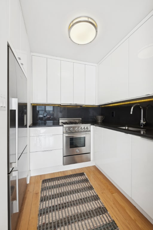 kitchen with sink, white cabinetry, light hardwood / wood-style flooring, and high end appliances