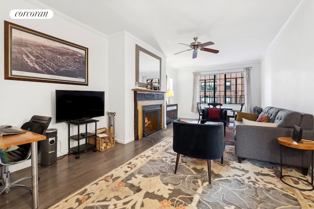 living area with a warm lit fireplace, wood finished floors, visible vents, a ceiling fan, and ornamental molding