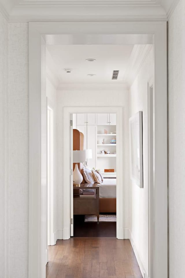 hall with visible vents, built in shelves, hardwood / wood-style floors, crown molding, and baseboards