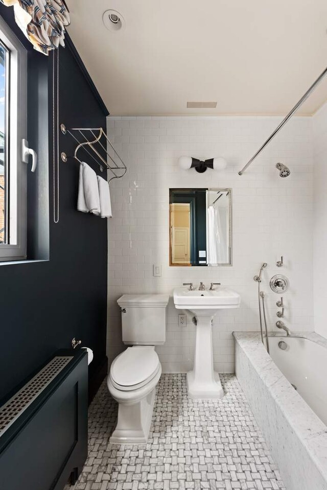 bathroom featuring shower / bathtub combination with curtain, tile patterned flooring, tile walls, and toilet