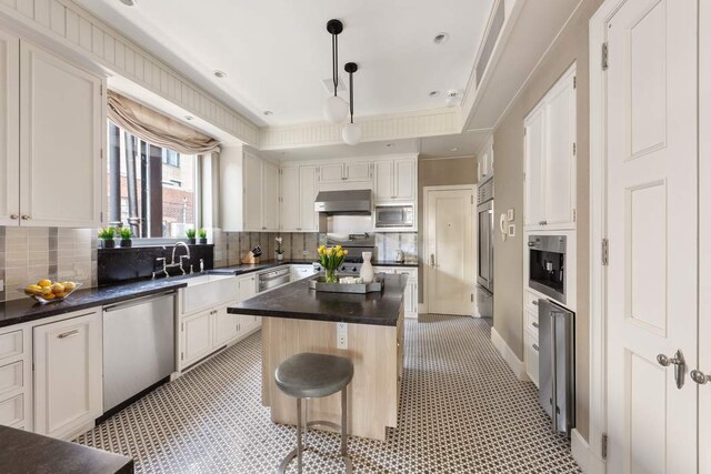 kitchen featuring built in appliances, decorative light fixtures, a kitchen island, white cabinets, and wall chimney range hood