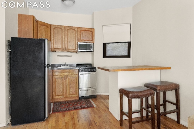 kitchen with light hardwood / wood-style floors, kitchen peninsula, a kitchen bar, sink, and appliances with stainless steel finishes