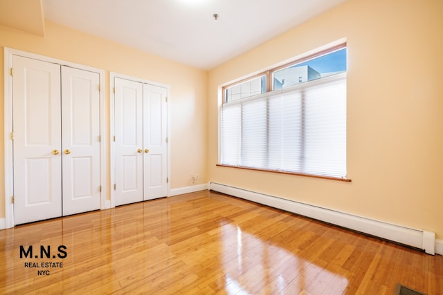 unfurnished bedroom with baseboards, baseboard heating, two closets, and wood finished floors