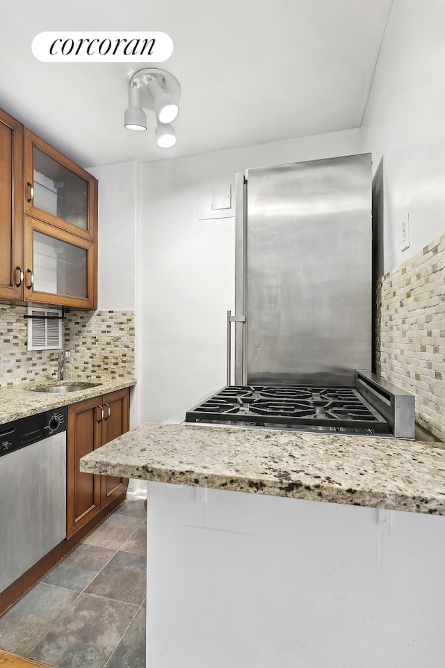 kitchen with tasteful backsplash, brown cabinetry, glass insert cabinets, stainless steel appliances, and a sink