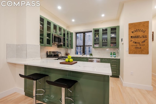 kitchen with stainless steel appliances, tasteful backsplash, a kitchen breakfast bar, kitchen peninsula, and green cabinetry