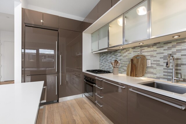 75 Wall St Unit 31P, New York City, NY 10005 - kitchen with appliances with stainless steel finishes, a sink, light wood-type flooring, light countertops, and decorative backsplash
