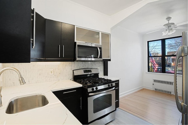 kitchen featuring radiator heating unit, stainless steel appliances, ceiling fan, sink, and light stone counters