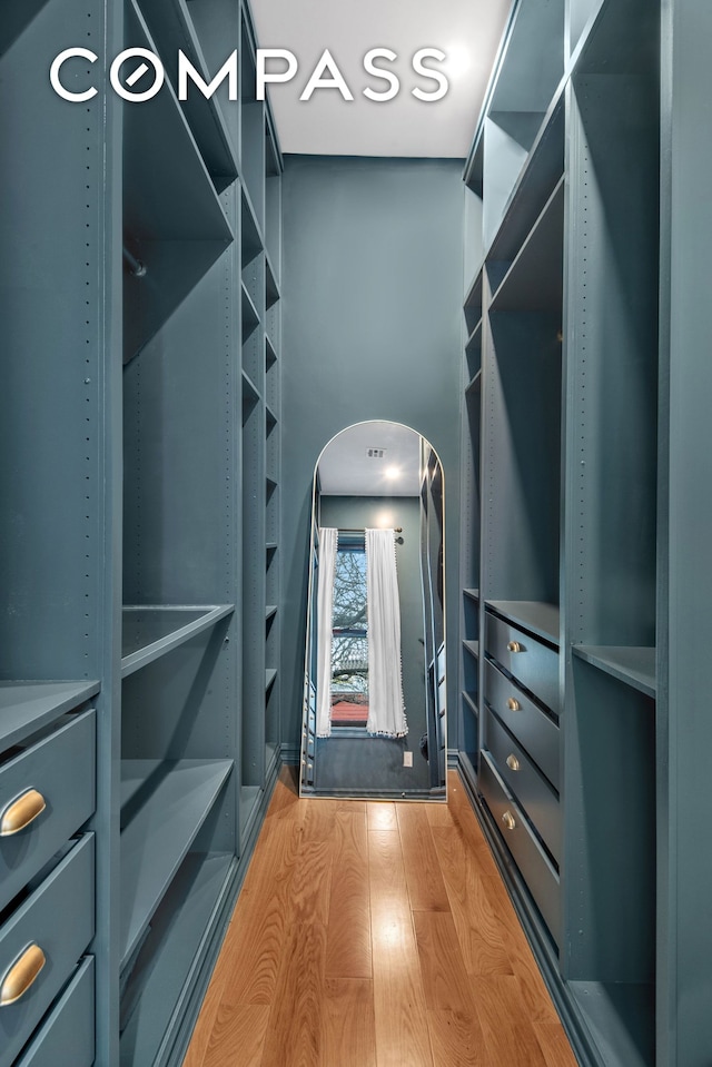 spacious closet with light wood-type flooring and arched walkways