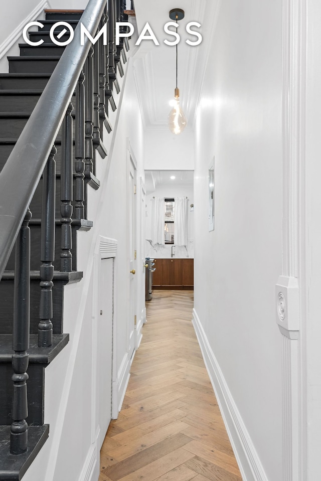 hall with crown molding, baseboards, light wood-style floors, and stairway