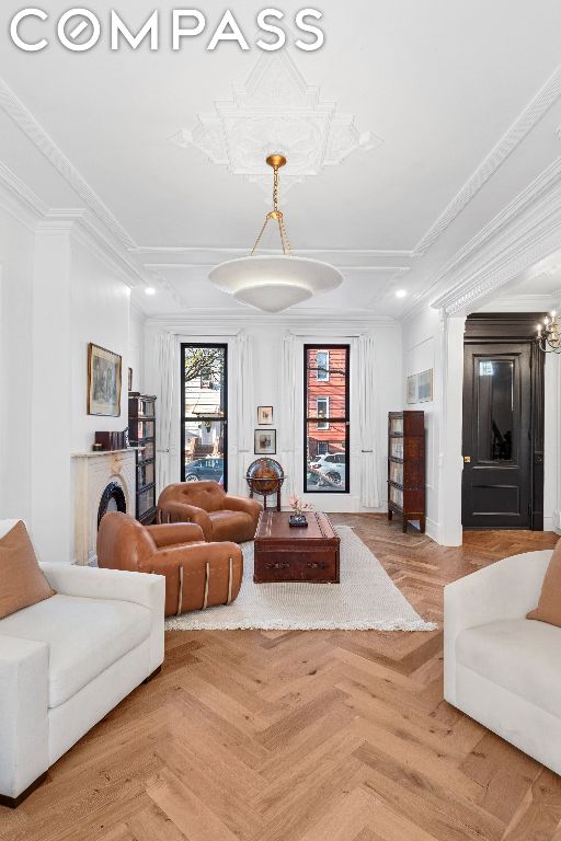 living room with an inviting chandelier, ornamental molding, and light parquet flooring