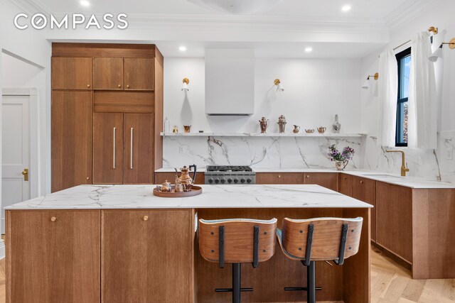 kitchen featuring ventilation hood, brown cabinets, a sink, range, and ornamental molding