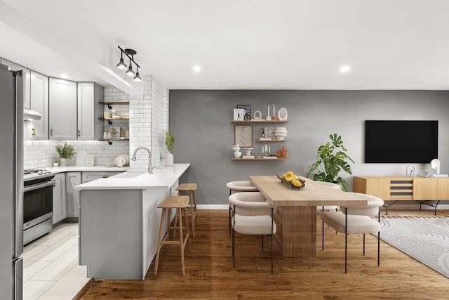 kitchen featuring kitchen peninsula, sink, a kitchen breakfast bar, gray cabinetry, and stainless steel range with electric stovetop