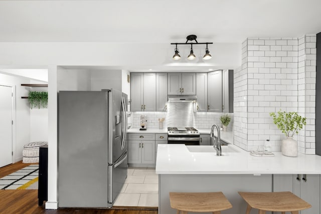 kitchen featuring kitchen peninsula, appliances with stainless steel finishes, decorative backsplash, a kitchen breakfast bar, and sink