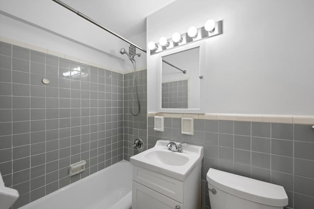 full bathroom featuring toilet, tiled shower / bath combo, tile walls, and vanity