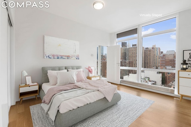 bedroom featuring a city view, a wall of windows, and wood finished floors